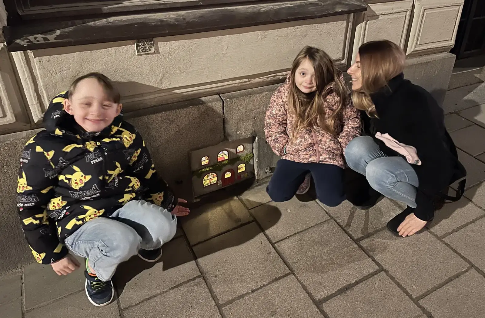 Children and an adult crouching beside Bamse's miniature house in Södermalm