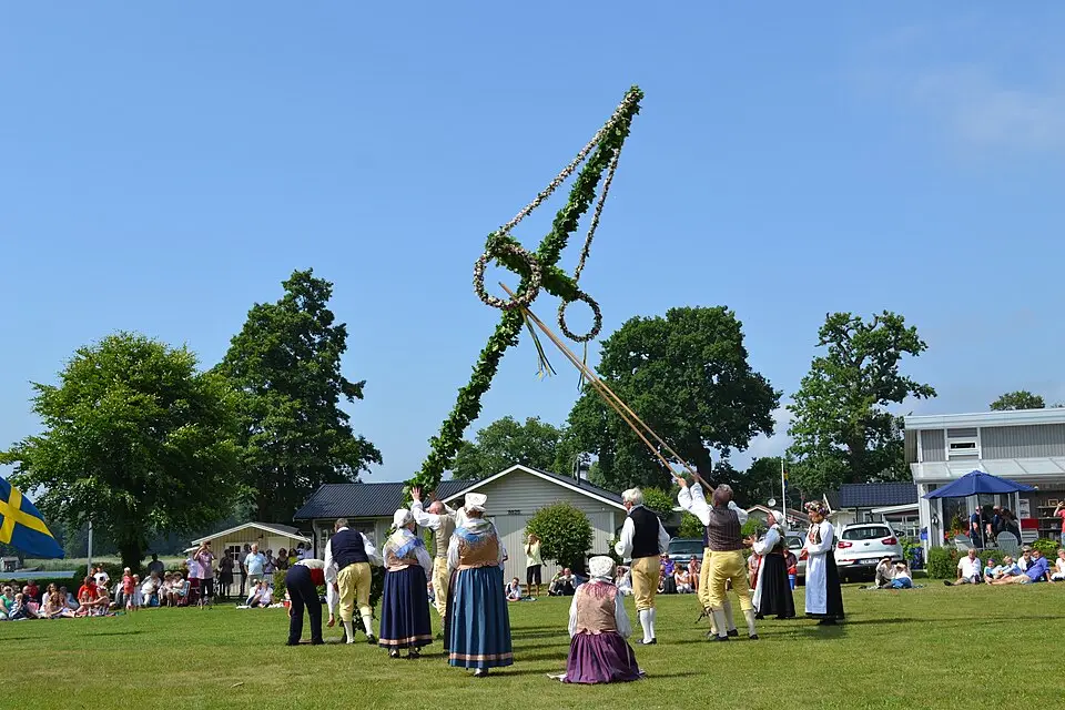 People raising a decorated Midsommar maypole during an outdoor celebration in Sweden