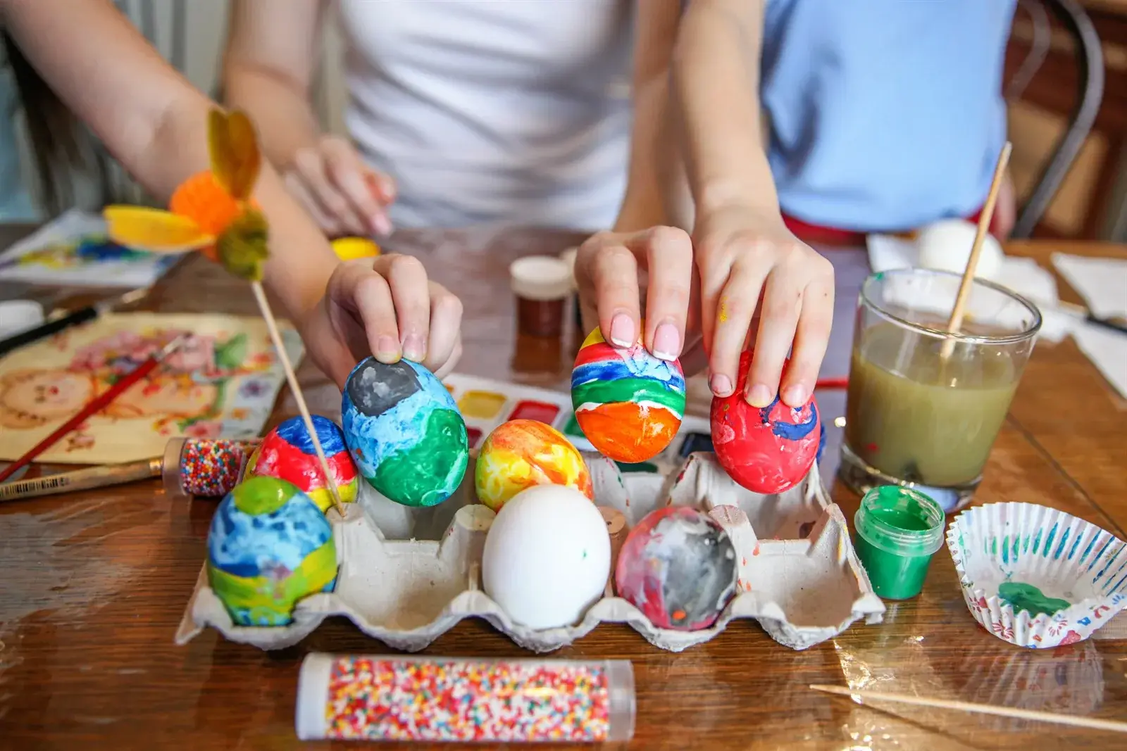 Hands decorating colorful Easter eggs at a table during Swedish Easter preparations