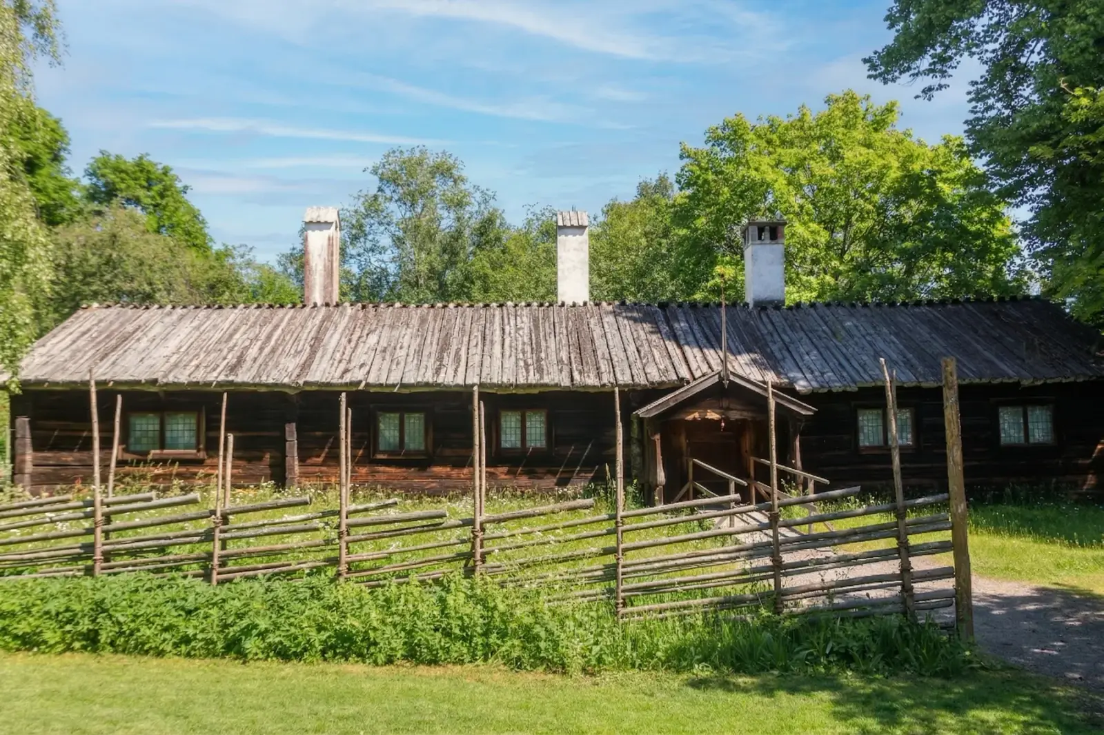 Traditional wooden farmstead at Skansen behind a rustic fence on a sunny day
