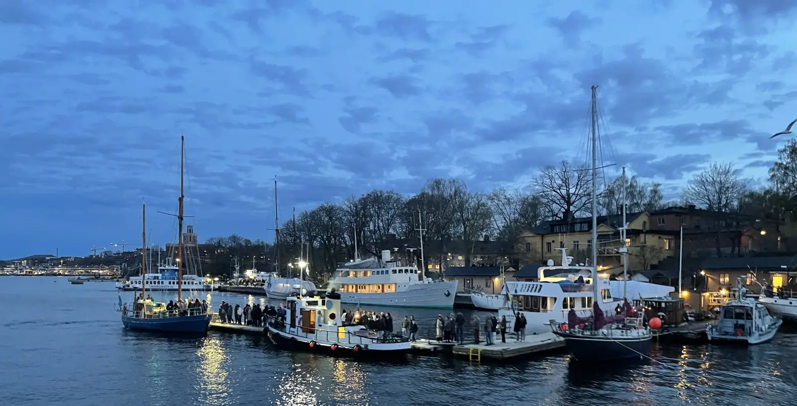 Blue-hour view of boats moored along a lit quay near Skeppsholmen in Stockholm