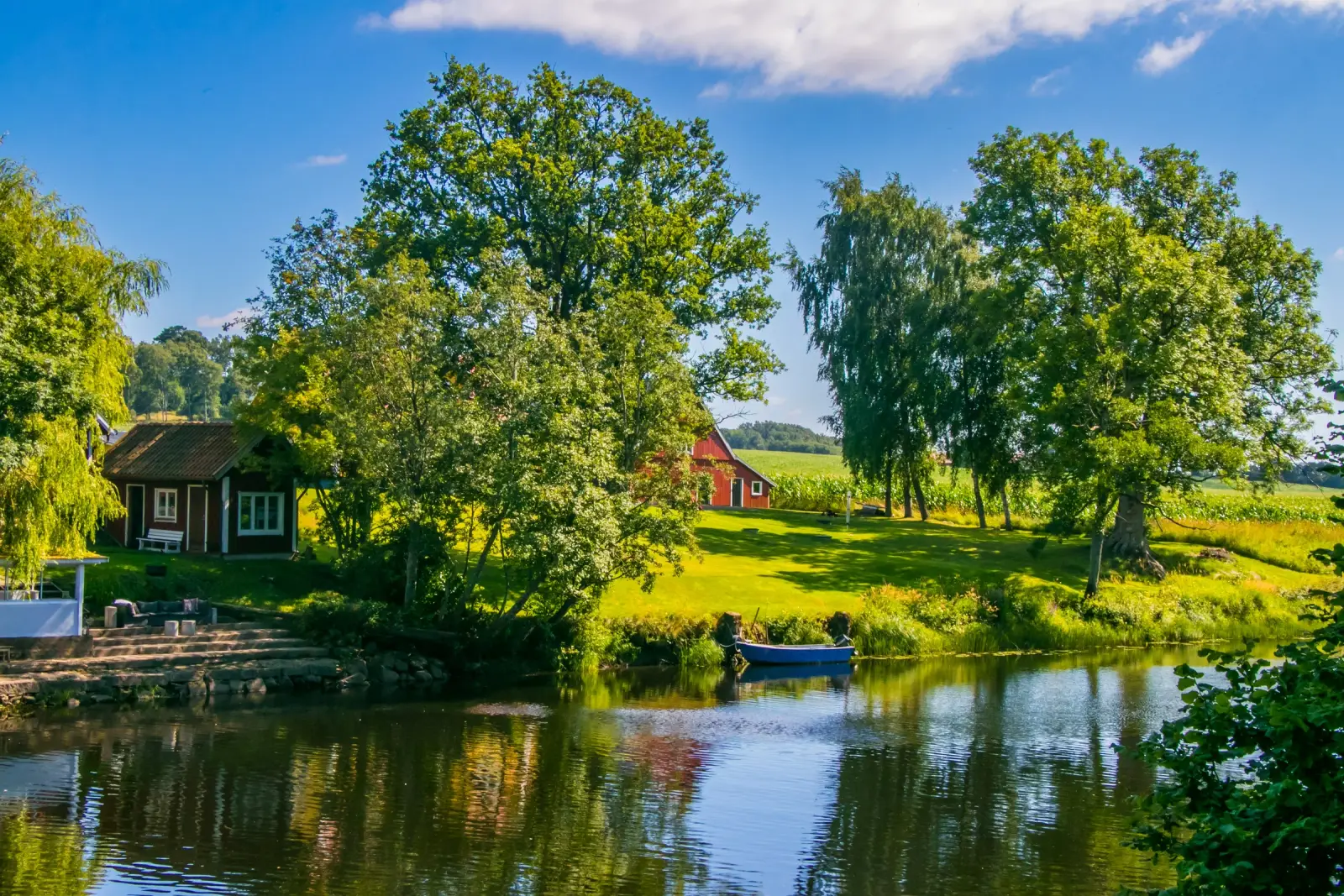 Calm archipelago shoreline with trees, red cottages, and a small boat on the water