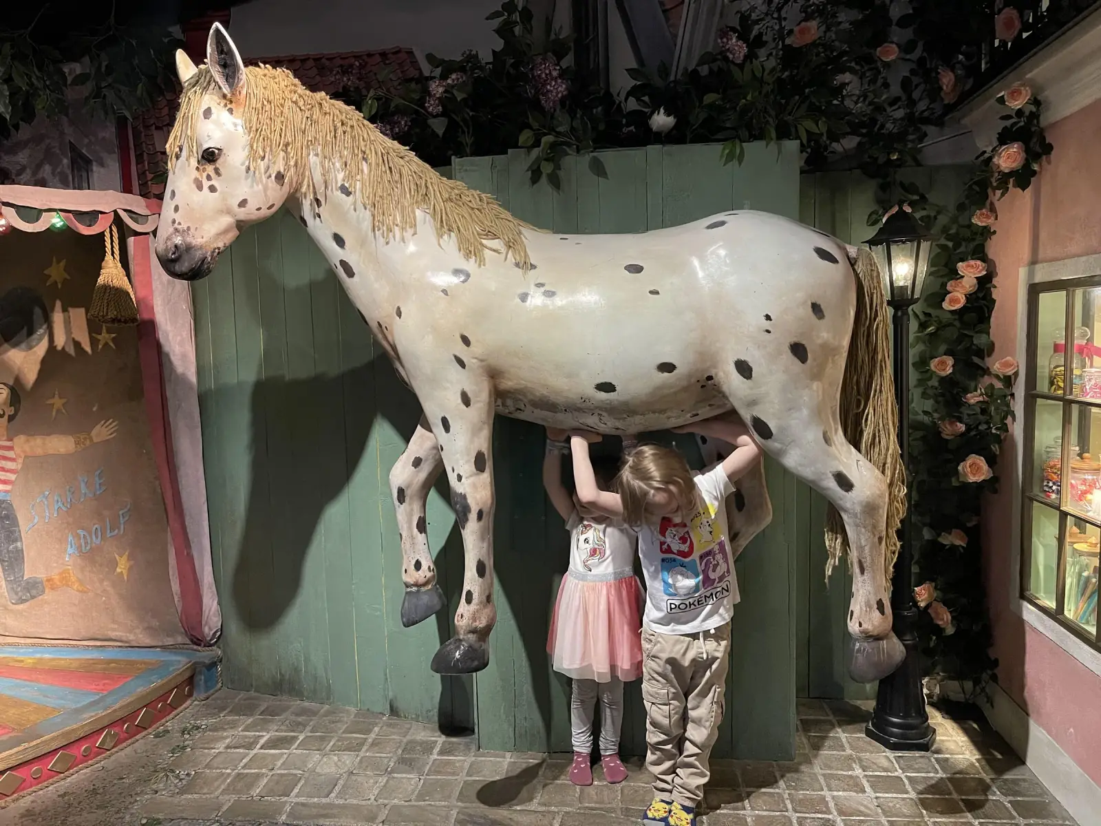 Two children standing beneath Junibacken's spotted horse in Stockholm