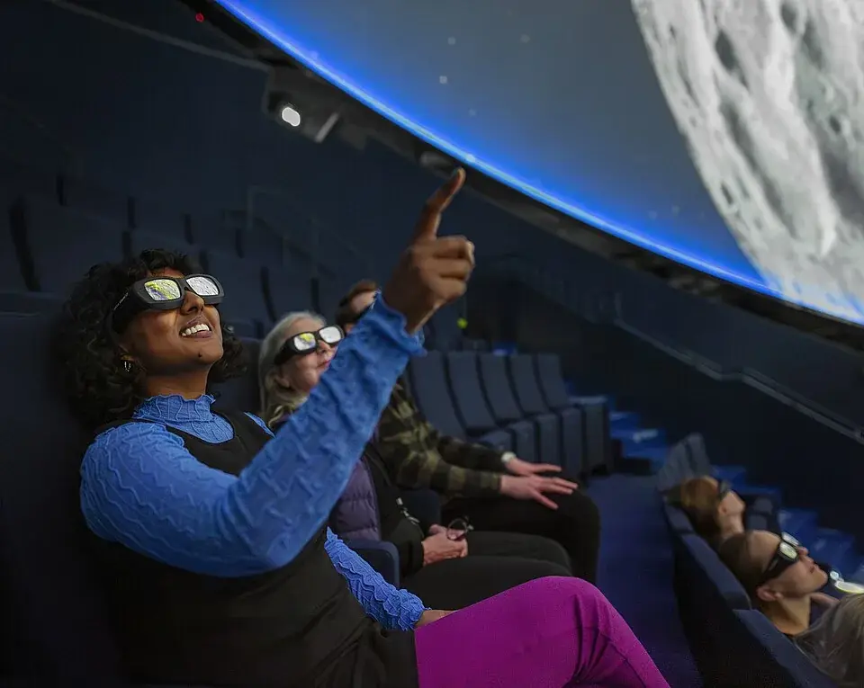 Visitors wearing 3D glasses inside Wisdome Stockholm beneath a large dome projection