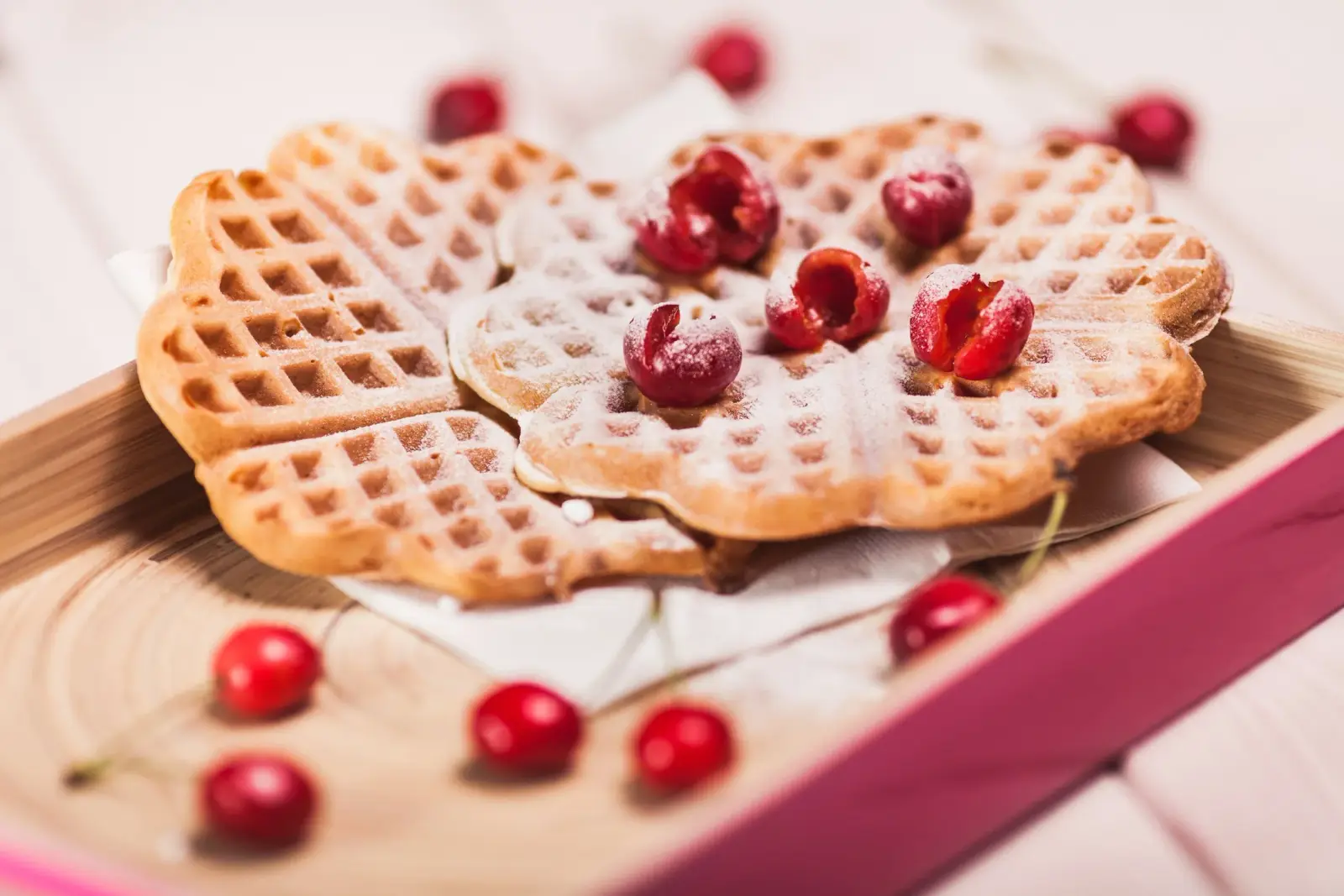 Heart-shaped Swedish waffles dusted with sugar and topped with red berries on a serving tray